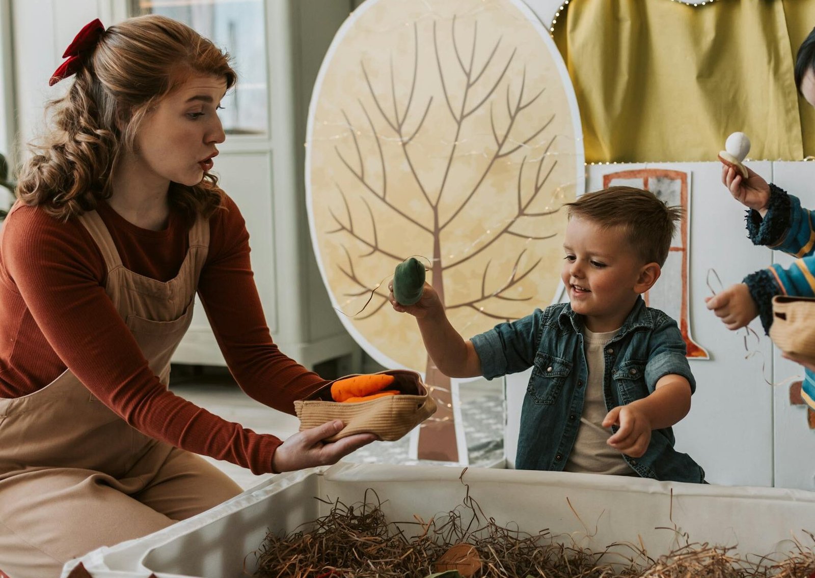 Two children and a woman play with puppets indoors, enjoying creative play with nature-themed decor.